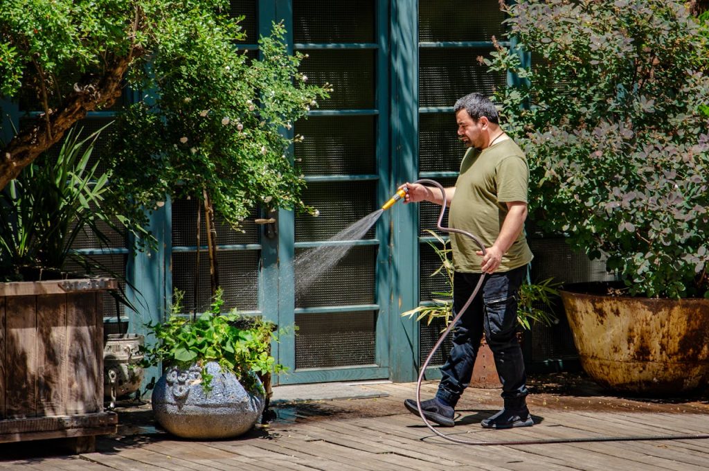 A man attentively waters plants on a sunny garden patio, emphasizing outdoor care and greenery.